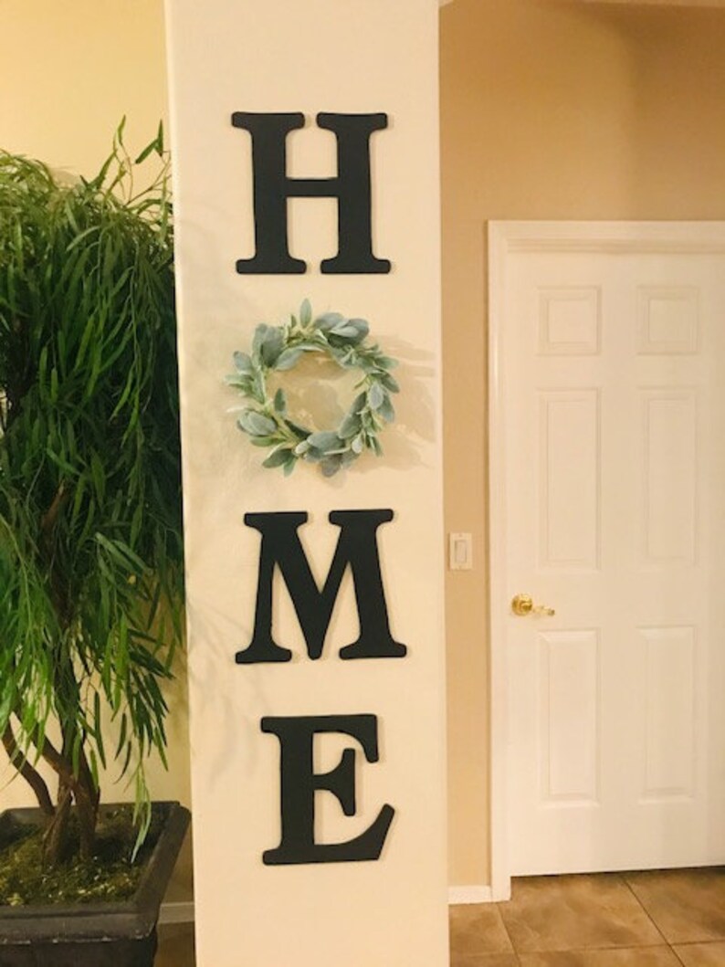 There Is A Kitchen Sign On The Wall Next To A Wreath And Table With Two